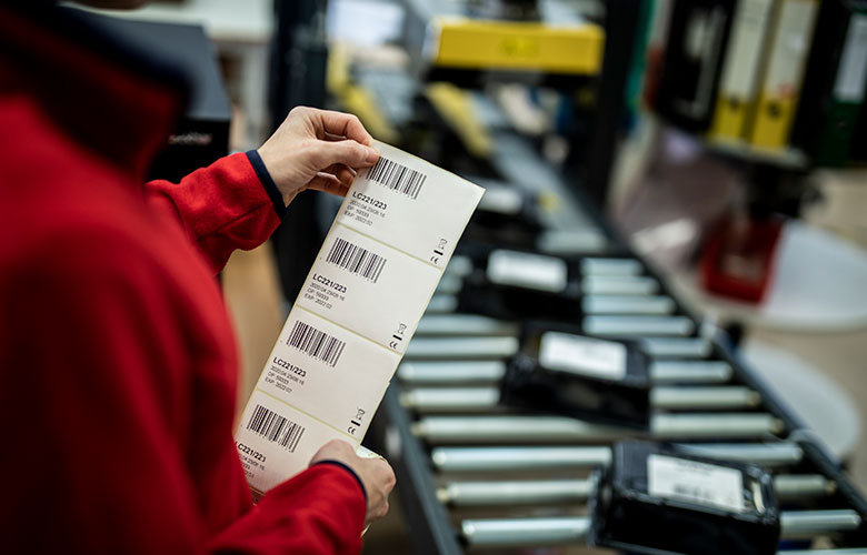 En arbeider fester etiketter på produkter som ligger på et samlebånd