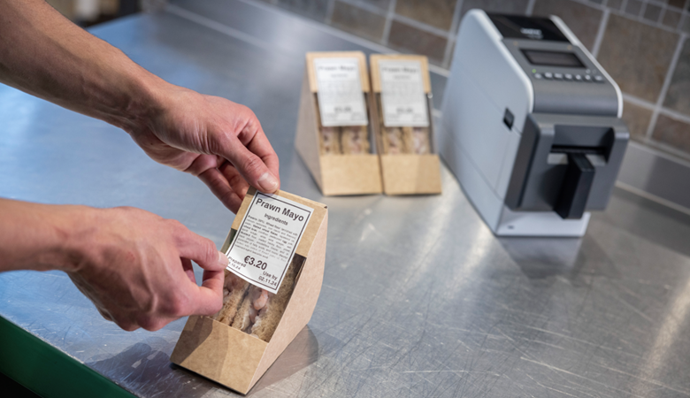 En Brother linerless etikettskriver skriver ut etiketter for å merke smørbrødpakker