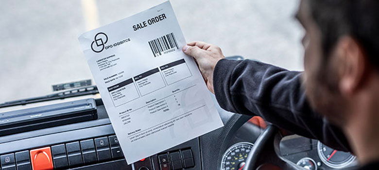 En mann holder et leveransedokument i hånden som er skrevet ut på en Brother PJ mobil skriver som er fastmontert i bilen