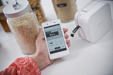 En person skriver ut merkelapper på en Brother PTP300BT CUBE merkemaskin via mobiltelefonen