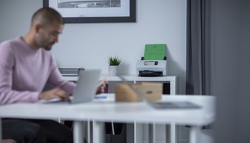Mann som sitter å jobber på en pc med en skanner i bakgrunnen